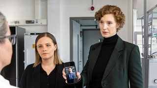 Szenenbild Tatort „Solange du atmest“ aus Bremen: Die Ermittlerinnen Moormann und Selb stehen einer Frau gegenüber und zeigen ein Foto eines Mannes auf Selbs Handy (Foto: ard-foto s2-intern/extern, Radio Bremen / Claudia Konerding) Szenenbild Tatort „Solange du atmest“ aus Bremen: Die Ermittlerinnen Moormann und Selb stehen einer Frau gegenüber und zeigen ein Foto eines Mannes auf Selbs Handy