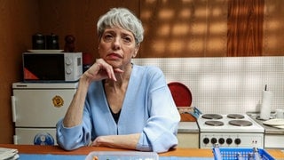 Szenenbild Tatort „Solange du atmest“ aus Bremen: Gerichtsmedizinerin Bingley sitzt am Tisch in einer kleinen Küche (Foto: ard-foto s2-intern/extern, Radio Bremen / Claudia Konerding) Szenenbild Tatort „Solange du atmest“ aus Bremen: Gerichtsmedizinerin Bingley sitzt am Tisch in einer kleinen Küche