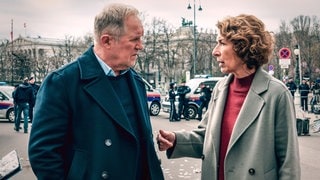 Szenenbild aus dem Tatort „Wir sind nicht zu fassen!“: Moritz Eisner und Bibi Fellner diskutieren auf der Straße in Wien miteinander, im Hintergrund Polizeiwagen (Foto: ard-foto s3, ORF/Petro Domenigg) Szenenbild aus dem Tatort „Wir sind nicht zu fassen!“: Moritz Eisner und Bibi Fellner diskutieren auf der Straße in Wien miteinander, im Hintergrund Polizeiwagen