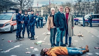 Szenenbild aus dem Tatort „Wir sind nicht zu fassen!“ aus Wien: Die Ermittler Meret Schande, Moritz Eisner, Bibi Fellner und Polizisten stehen auf der Straße vor einem am Boden liegenden jungen Mann (Foto: ard-foto s3, ORF/Petro Domenigg) Szenenbild aus dem Tatort „Wir sind nicht zu fassen!“ aus Wien: Die Ermittler Meret Schande, Moritz Eisner, Bibi Fellner und Polizisten stehen auf der Straße vor einem am Boden liegenden jungen Mann