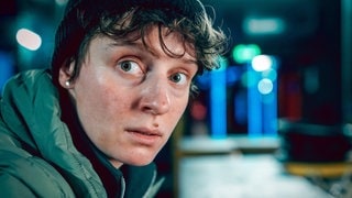 Szenenbild aus dem Tatort „Wir sind nicht zu fassen!“ aus Wien: Das Gesicht der Aktivistin Katja Ralko in abendlicher städtischer Umgebung (Foto: ard-foto s3, ORF/Petro Domenigg) Szenenbild aus dem Tatort „Wir sind nicht zu fassen!“ aus Wien: Das Gesicht der Aktivistin Katja Ralko in abendlicher städtischer Umgebung