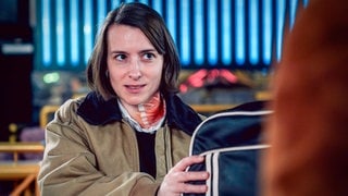 Szenenbild aus dem Tatort „Wir sind nicht zu fassen!“ aus Wien: BK-Ermittlerin Meret Schande mit blutigem Halsverband hält Tasche fest (Foto: ard-foto s3, ORF/Petro Domenigg) Szenenbild aus dem Tatort „Wir sind nicht zu fassen!“ aus Wien: BK-Ermittlerin Meret Schande mit blutigem Halsverband hält Tasche fest