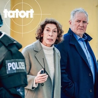 Szenenbild aus dem Tatort „Wir sind nicht zu fassen!“ aus Wien: Die Ermittler Moritz Eisner und Bibi Fellner zwischen zwei bewaffneten Polizisten