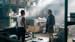 Szenenbild aus dem Tatort „Feuer“ aus Dortmund: Zwei Männer, einer davon Faber, stehen sich in einem Lagerhaus mit Sofas und Aktenbergen gegenüber. Die Atmosphäre wirkt angespannt und geheimnisvoll. (Foto: ard-foto s2-intern/extern, WDR/Martin Rottenkolber) Szenenbild aus dem Tatort „Feuer“ aus Dortmund: Zwei Männer, einer davon Faber, stehen sich in einem Lagerhaus mit Sofas und Aktenbergen gegenüber. Die Atmosphäre wirkt angespannt und geheimnisvoll.