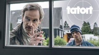 Szenenbild aus dem Tatort „Feuer“ aus Dortmund: Kommissar Faber schaut mit erhobenem Zeigefinger durch ein Fenster.