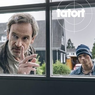 Szenenbild aus dem Tatort „Feuer“ aus Dortmund: Kommissar Faber schaut mit erhobenem Zeigefinger durch ein Fenster.