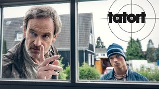 Szenenbild aus dem Tatort „Feuer“ aus Dortmund: Kommissar Faber schaut mit erhobenem Zeigefinger durch ein Fenster.