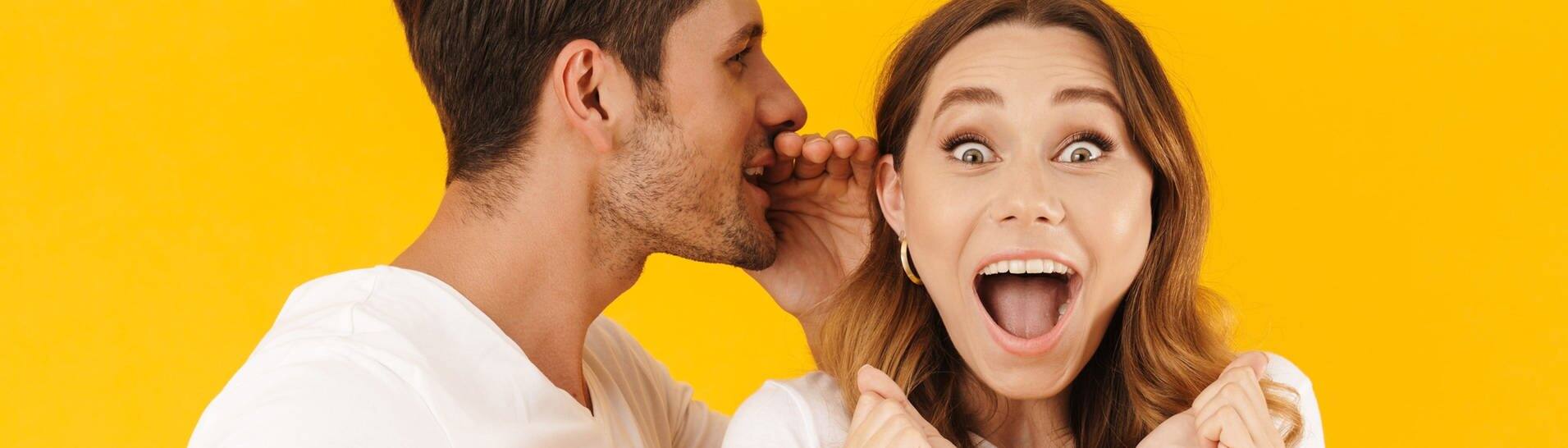 Junger Mann flüstert Frau etwas ins Ohr, sie freut sich (Foto: Adobe Stock/Drobot Dean)
