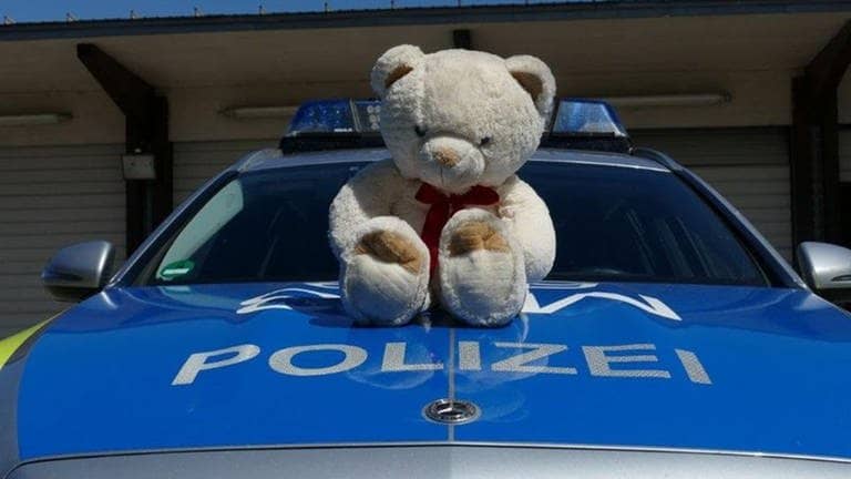 Ein Plüsch-Teddybär sitzt auf der Motorhaube eines Streifenwagens. (Foto: Pressestelle, Polizei Mannheim)
