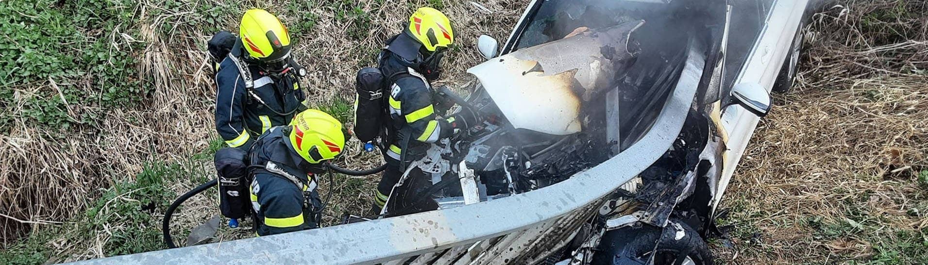 Feuerwehrleute der Freiwilligen Feuerwehr löschen den Brand nach dem schweren Autounfall in Österreich.