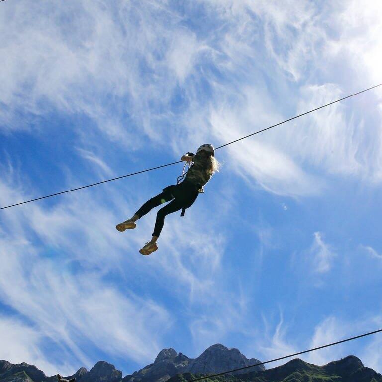 Eine junge Frau gleitet mit einer Seilrutsche vor blauem Himmel