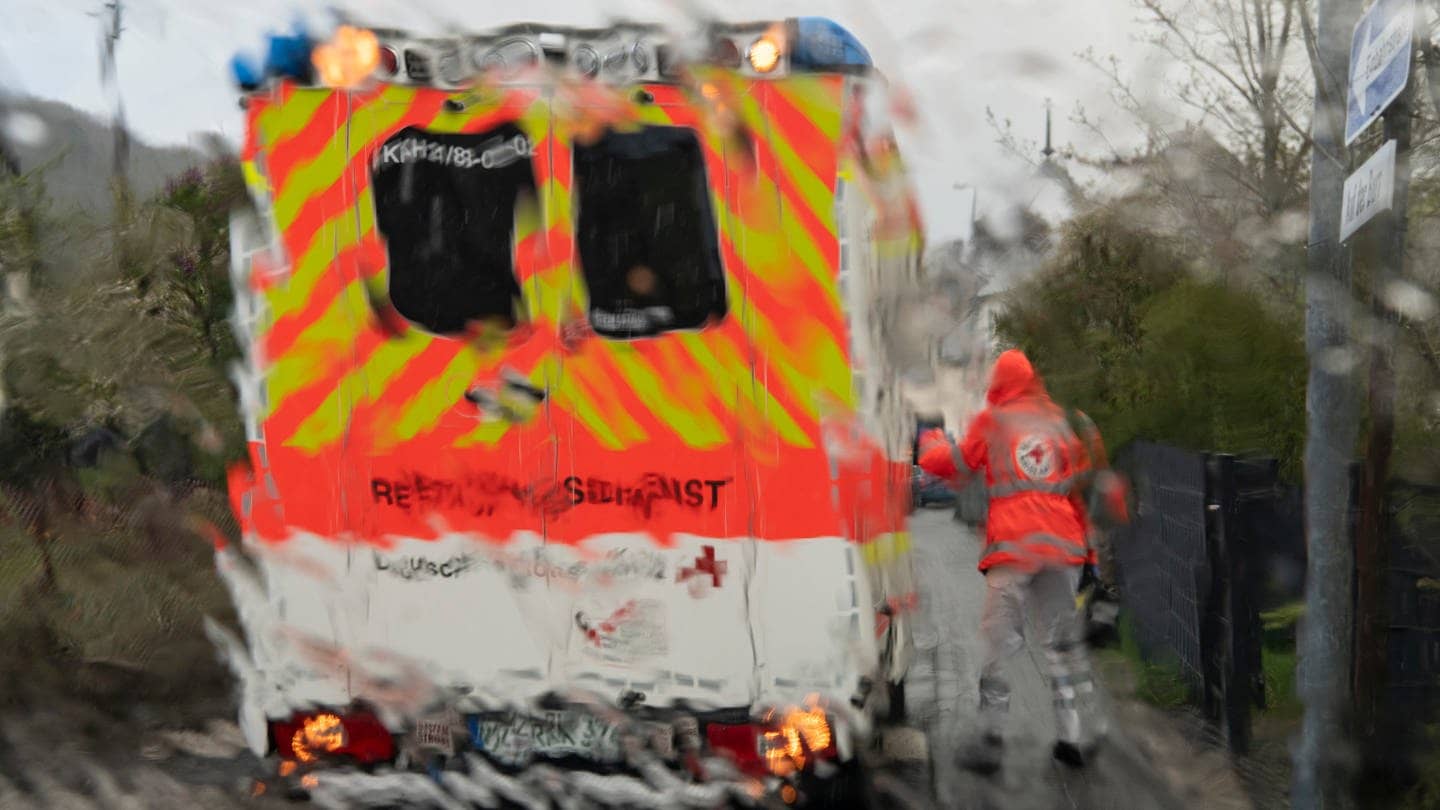 (Symbolbild) Im strömenden Regen geht ein Notfallsanitäter des Deutschen Roten Kreuzes (DRK) zu einem Rettungswagen, der vor dem Haus eines Patienten steht. 