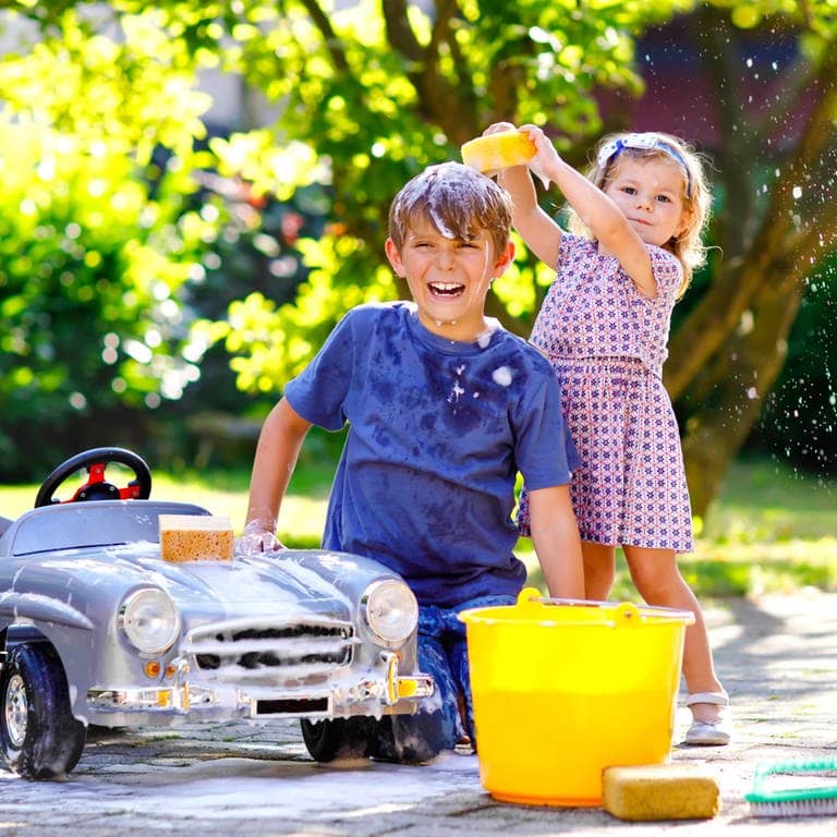 Junge und Mädchen beschäftigen sich an einem kleinen Auto mit der Autoreinigung. Symbolbild für Hausmittel, um das Auto nach dem Saharastaub zu waschen.