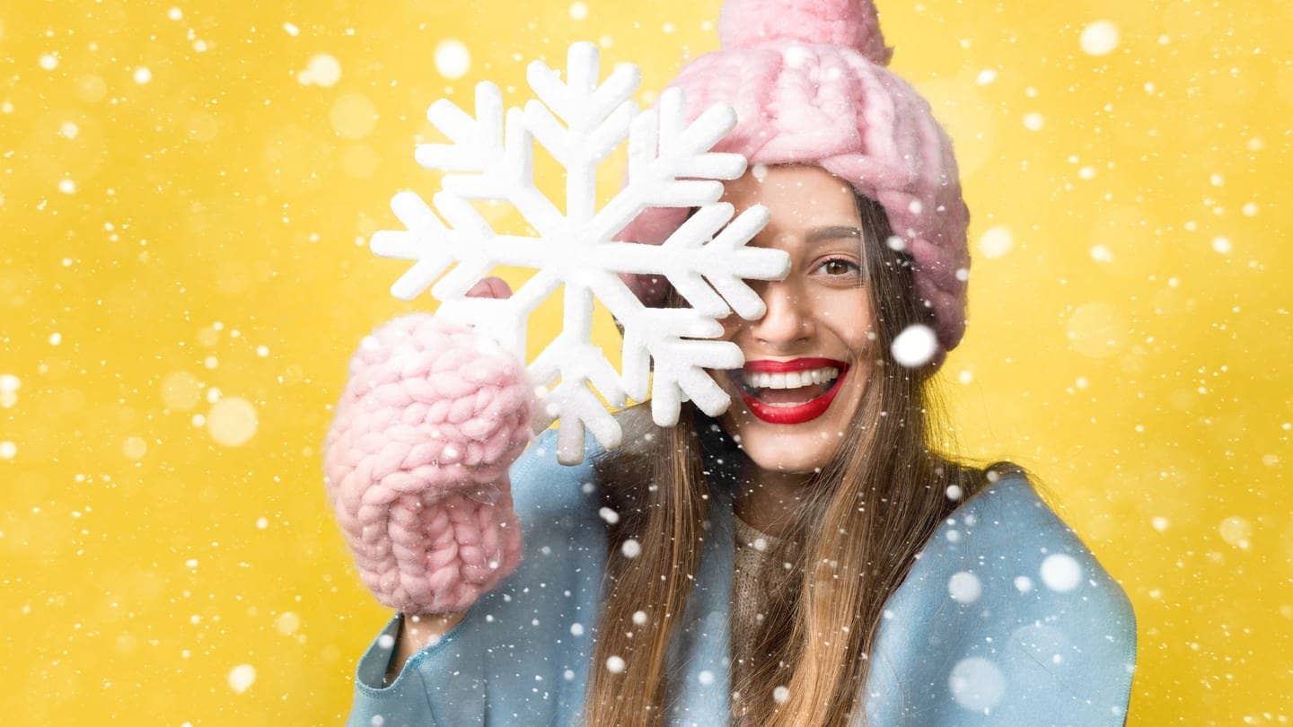 Junge Frau mit Handschuhen und Mütze, hält eine Schneeflocke hoch und lacht