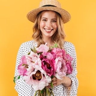 Junge Frau mit Sonnenhut und einem Strauß Blumen in der Hand. Symbolbild für Sprüche, mit denen wir es durch die Blume sagen können, offiziell freundlich.