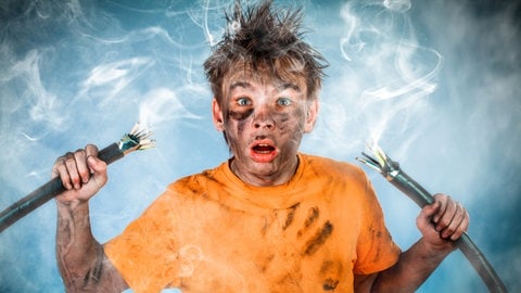 Junge hält zwei Stromkabel in der Hand, es gab eine kleine Explosion. Das Gesicht des Kindes ist voll mit Ruß und Staub. Symbolbild für die Frage: Haften Eltern für ihre Kinder oder nicht?