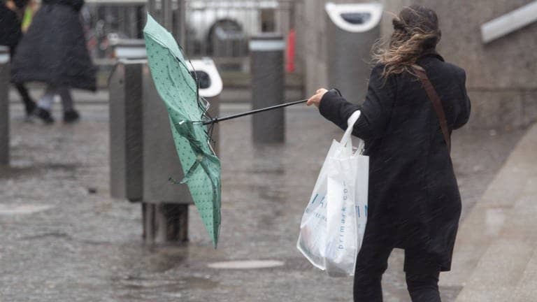 Frau läuft bei Sturm mit einem Regenschirm auf der Straße - Unwetter, Sturm und Schnee: Dieses Wetter erwartet uns jetzt in BW und RLP (Foto: IMAGO, IMAGO / NurPhoto)