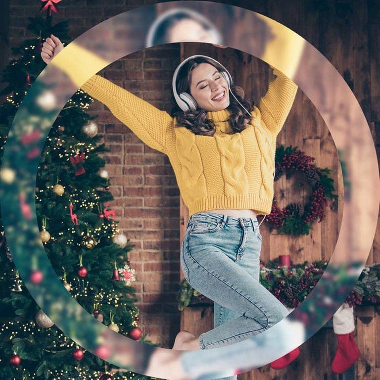 Eine junge Frau in einem gelben Pullover tanzt vor einem Weihnachtsbaum und hört Musik mit Kopfhörern. (Foto: Adobe Stock / deagreez)