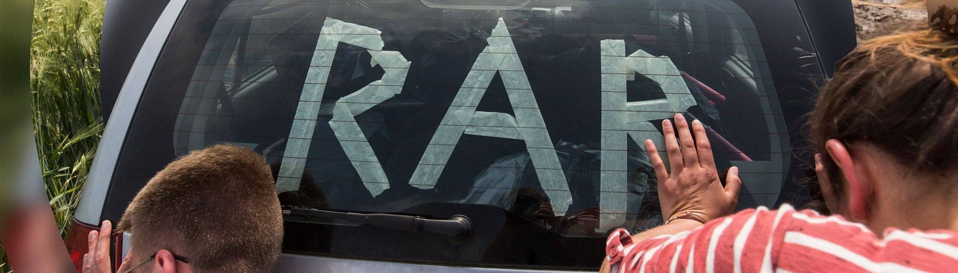 Rock am Ring: Zwei Menschen schieben ein Auto mit dem Schriftzug „RaR“.